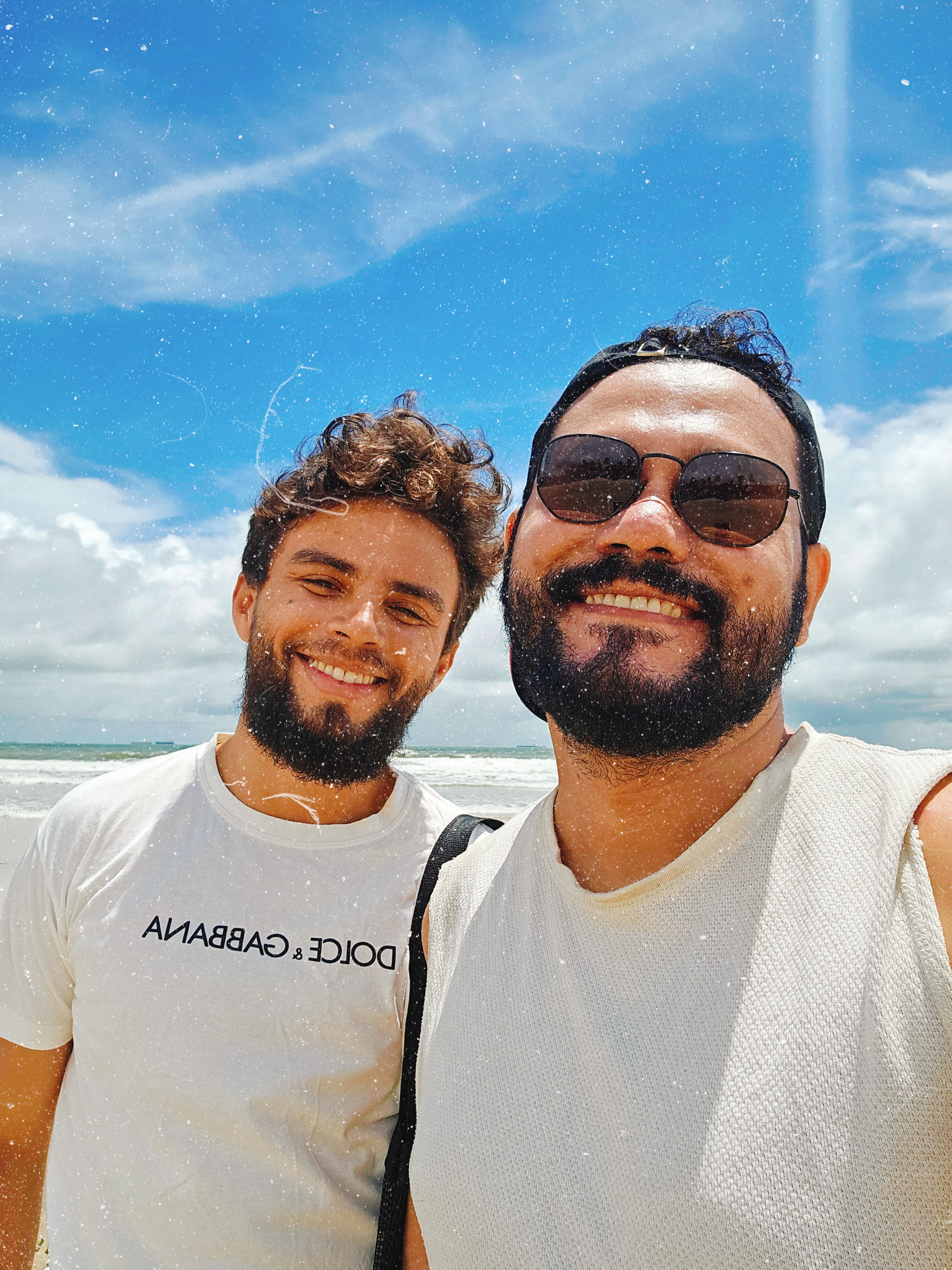 Venilson e Walterly sorrindo na praia sob céu azul